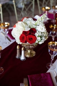 Table centerpiece for wedding dinner with burgundy velvet table runner under floral arrangement